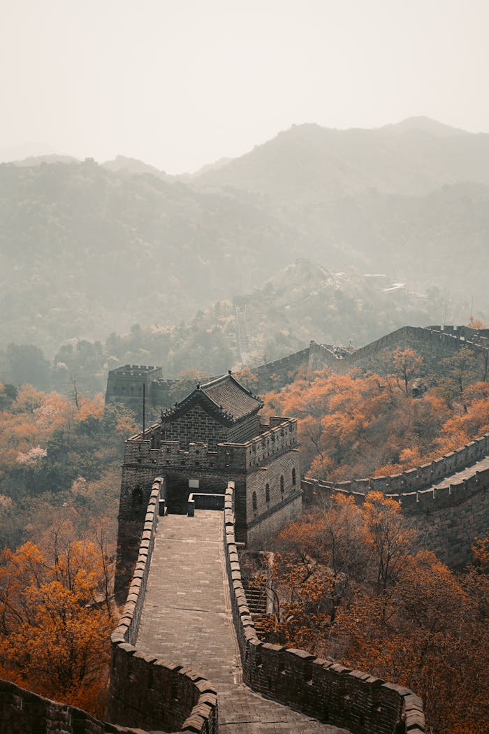 why-choose-us Scenic view of the Great Wall of China surrounded by autumn foliage and foggy mountains.
