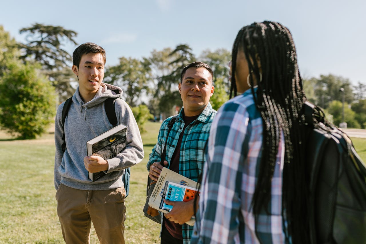 services-img Group of students chatting outdoors with books on a sunny day.
