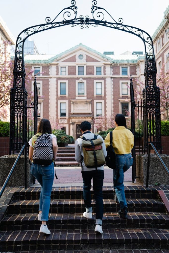 pexels photo 7972506 A group of students with backpacks walks towards a university building through an arch.