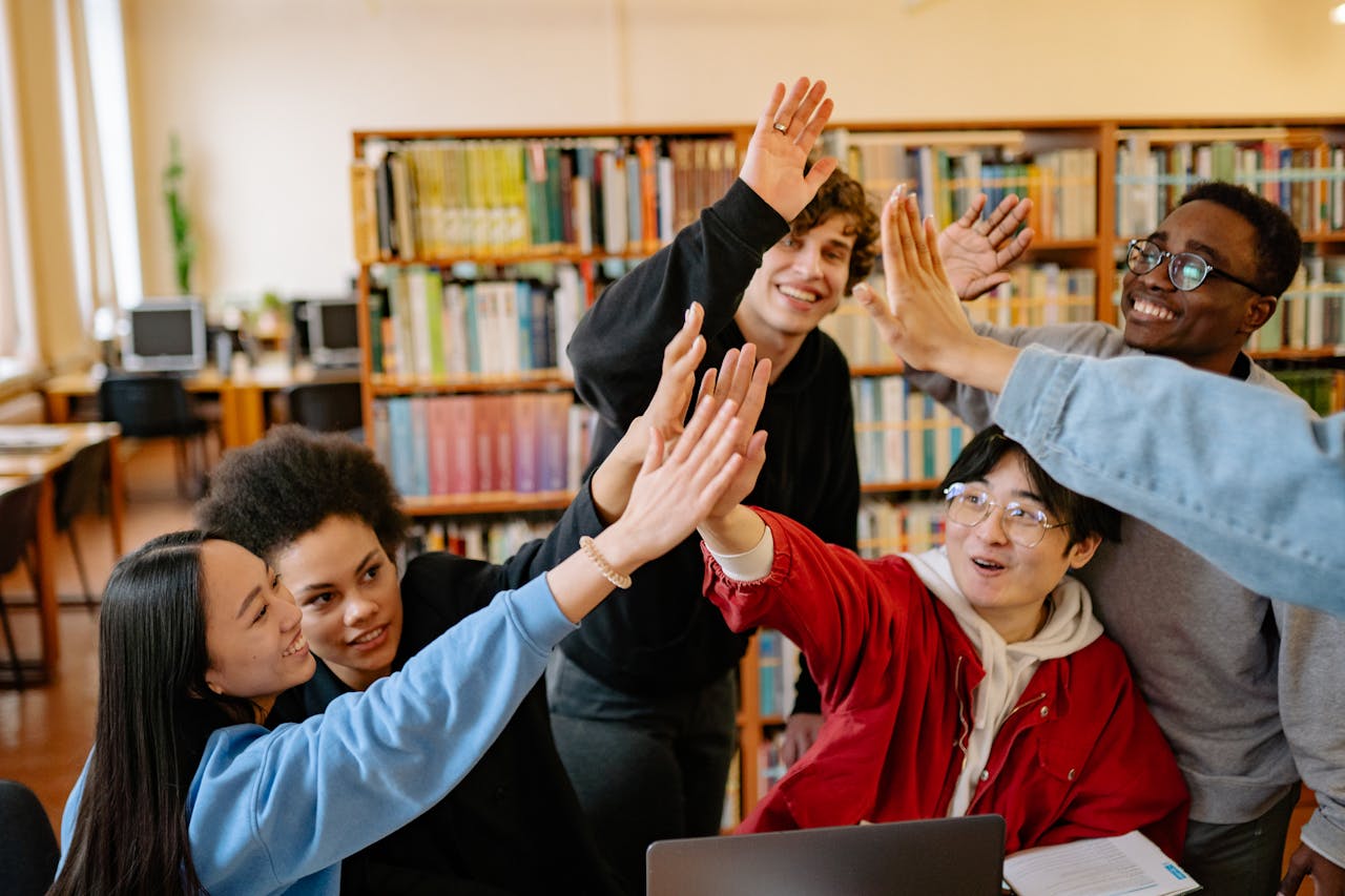 Cómo elegir la beca internacional ideal desde Latinoamérica Group of happy students high-fiving in a library setting, celebrating success.